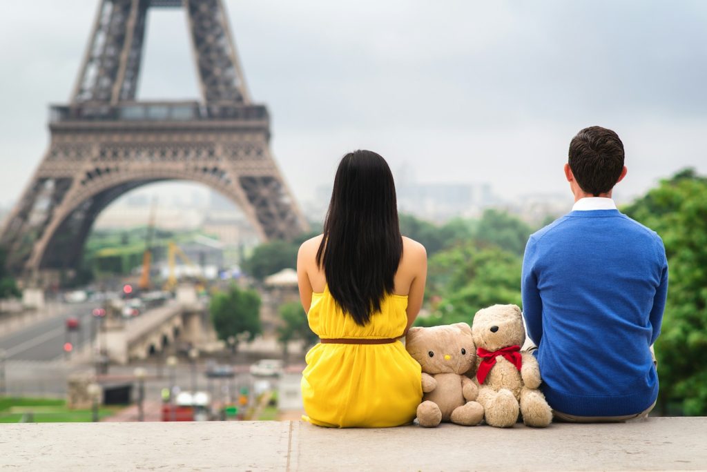 a man and a woman sitting on a ledge in front of the eiffel